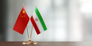 chinese and iranian flag pair on a desk over defocused background